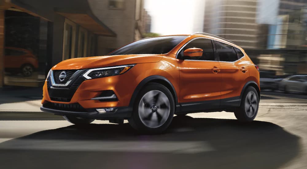 An orange 2020 Nissan Rogue Sport is shown driving in a city from a used Honda dealer.