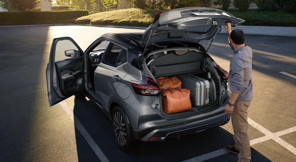 A man is putting cargo into the back of a grey 2023 Nissan Kicks.