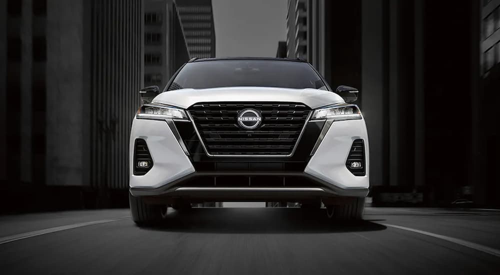 A white 2024 Nissan Kicks SR driving in a city towards a Nissan dealer near Oak Ridge.