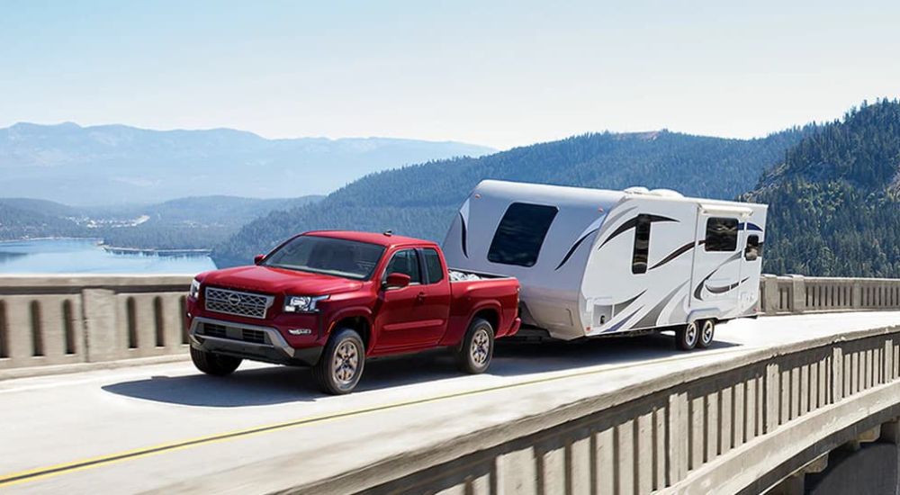 A red 2024 Nissan Frontier for sale is shown towing a trailer.