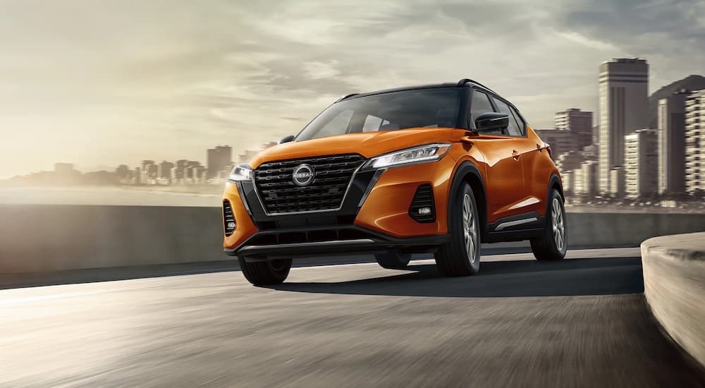 An orange 2024 Nissan Kicks driving across a bridge.