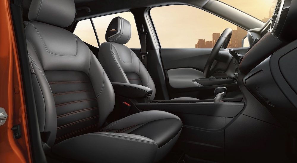 Side angle view of a the black interior cabin of an orange 2024 Nissan Kicks SV.
