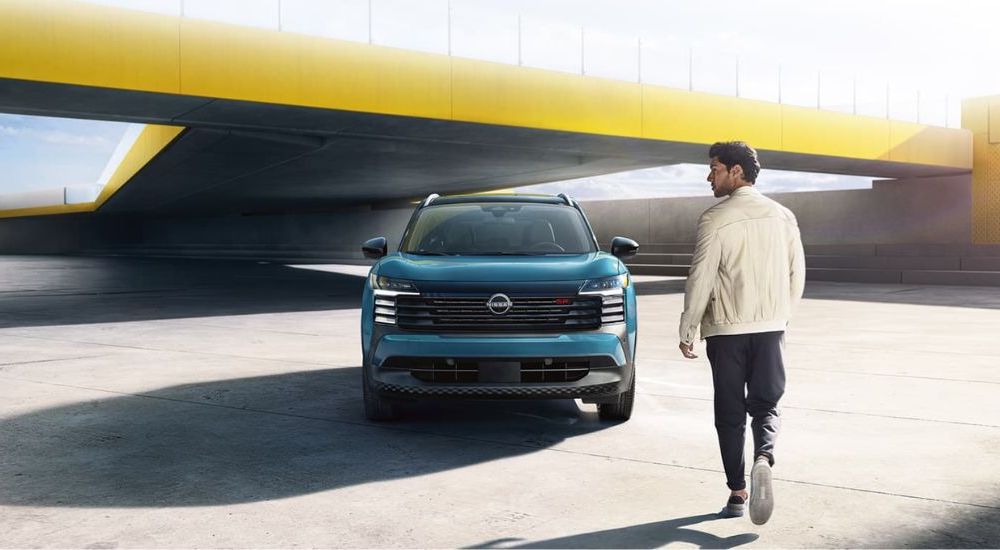 A man approaching a parked, front angled blue 2025 Nissan Kicks SR.