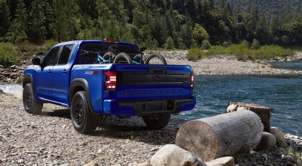 Rear view of a blue 2025 Nissan Frontier Pro-4X parked by a river.