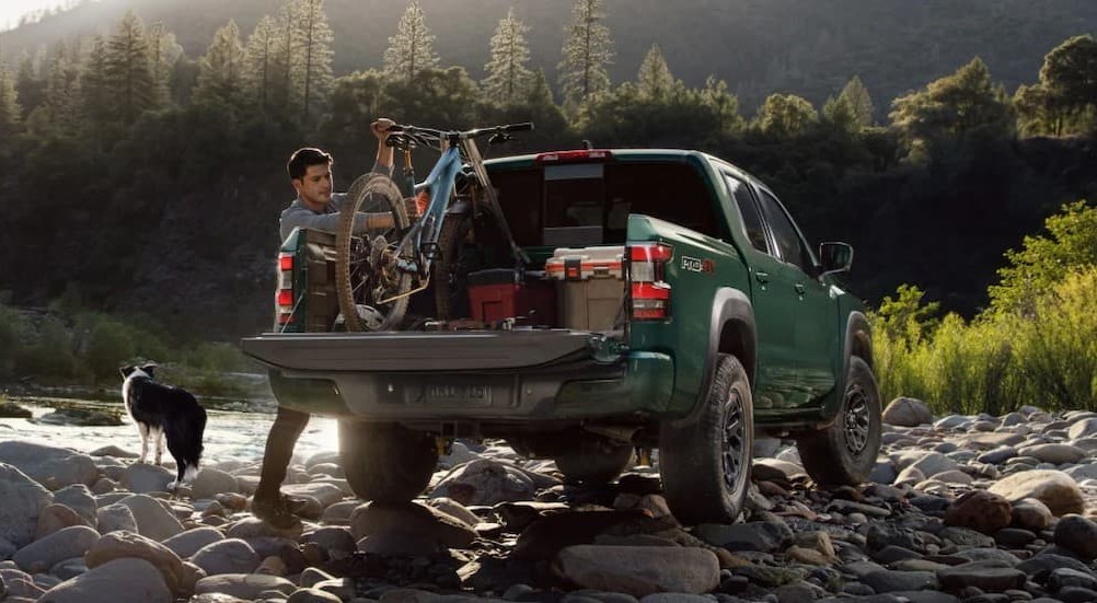 A person removing a bike from the bed of  green 2026 Nissan Frontier Pro-4X.