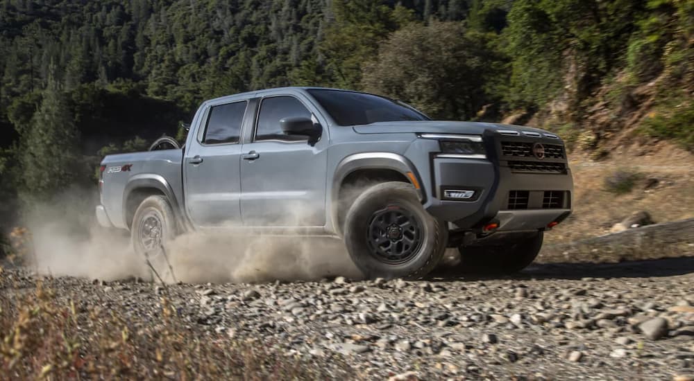 Grey 2026 Nissan Frontier Pro-4X driving off-road on a rocky path.