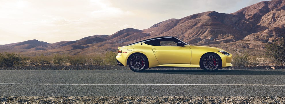 2024 Nissan Z in yellow driving on a desert road with mountains in the distance