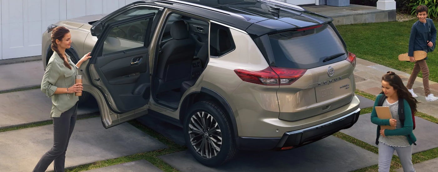 Rear of a tan 2026 Nissan Rogue parked on a driveway with an open door.