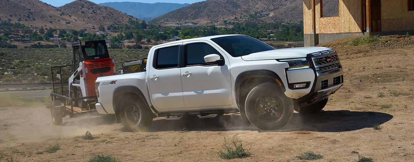 White 2026 Nissan Frontier towing a tractor trailer off-road.