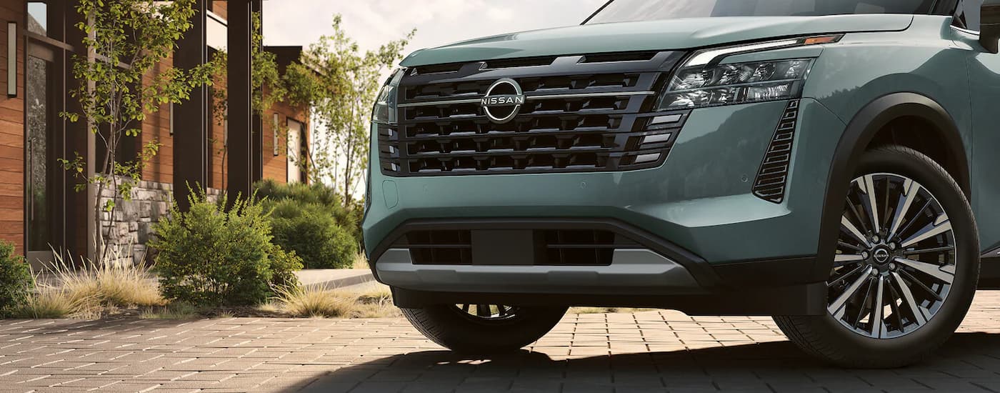 Close-up on the grille of a green 2026 Nissan Pathfinder parked on a driveway.