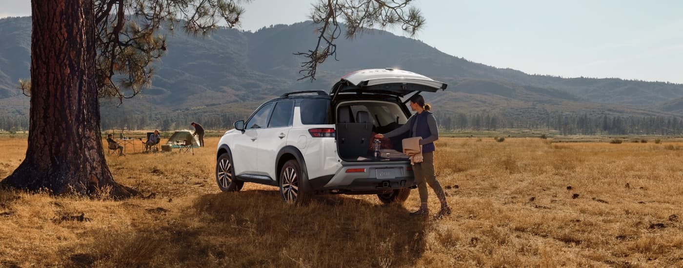 Person opening the hatch of a white 2026 Nissan Pathfinder parked off-road.