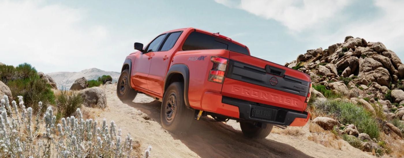 Rear view of a red 2026 Nissan Frontier driving off-road.