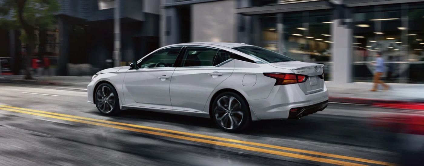 Side view of a white 2025 Nissan Altima SR driving on blurred city streets.