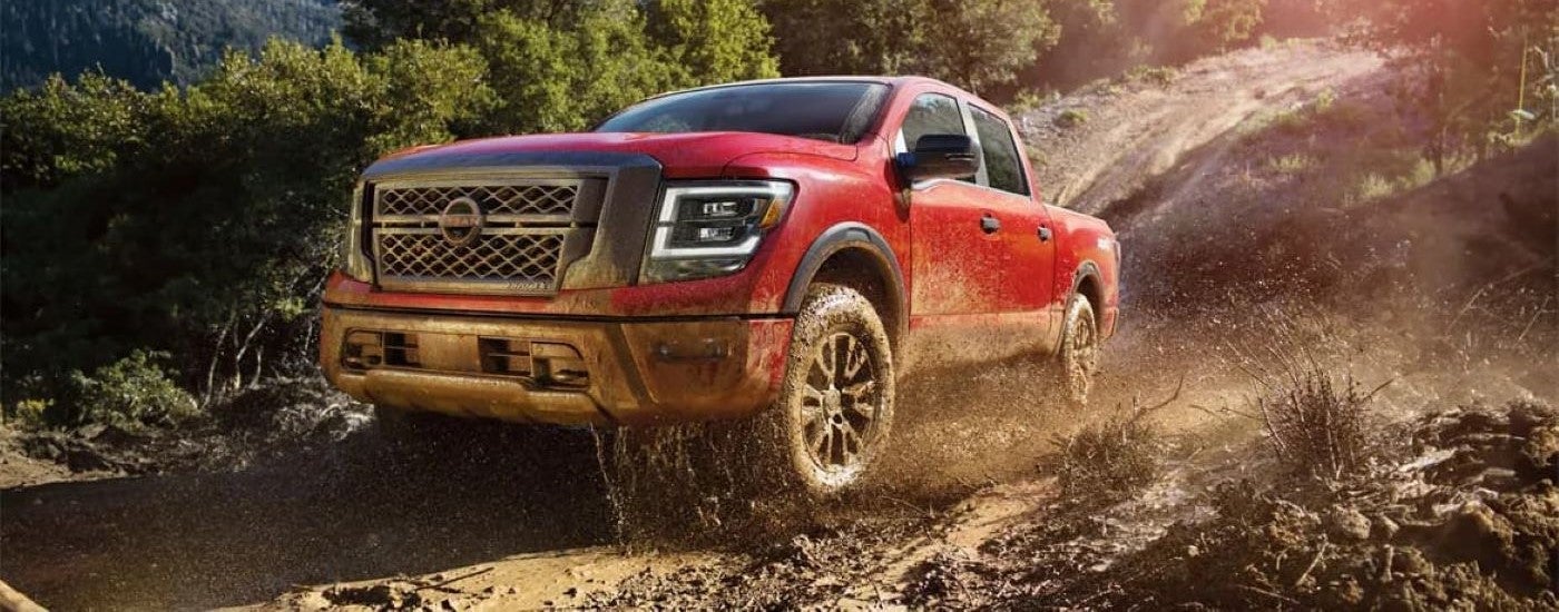 A red 2024 Nissan Titan is shown kicking up mud on a tree-lined trail.