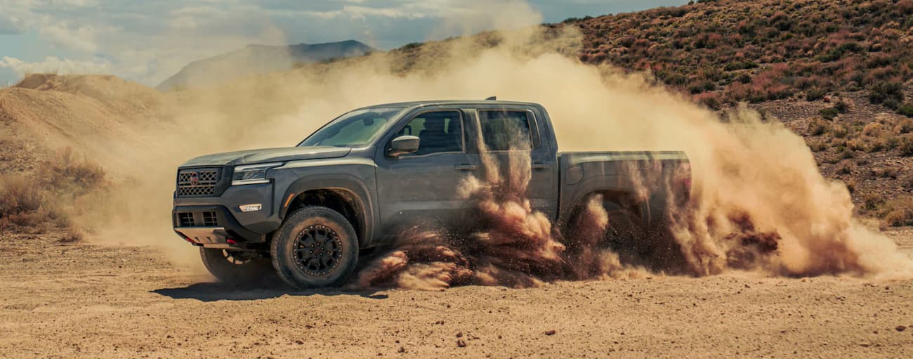 Side angle view of a grey 2022 Nissan Frontier driving off-road in a desert from a Nissan dealer near me.