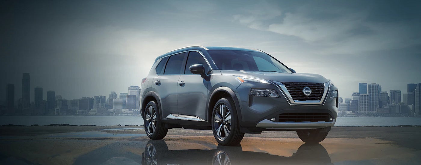 A silver 2024 Nissan Rogue parked in front of a city skyline.