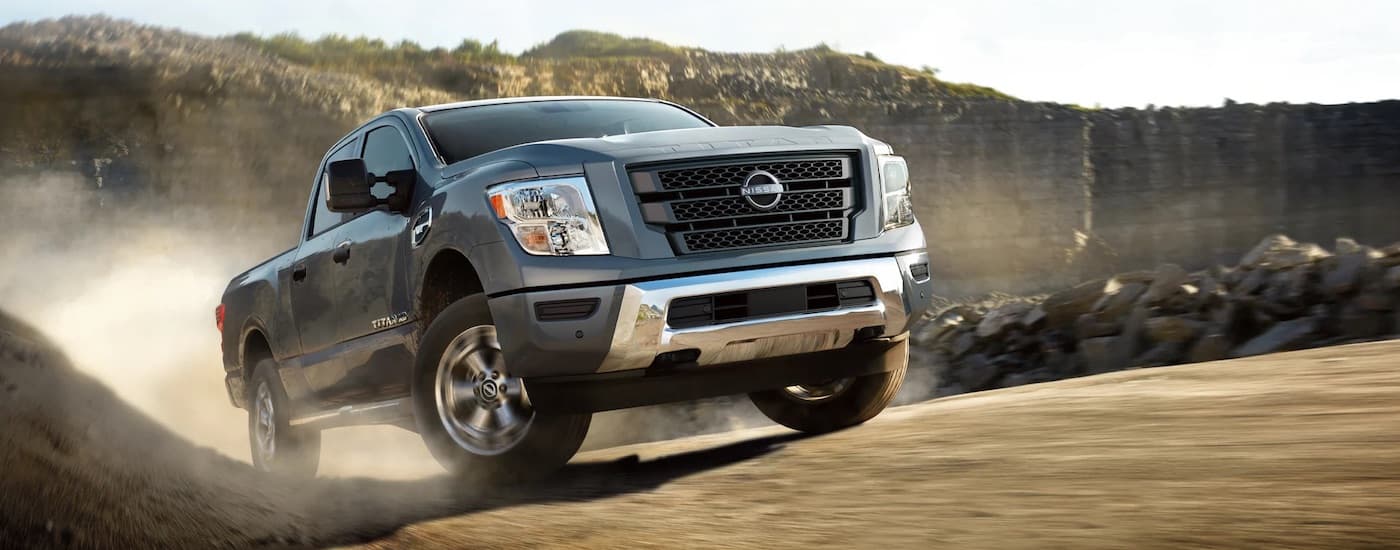 A grey 2024 Nissan Titan driving up a hill from a Nissan dealer near Oak Ridge.