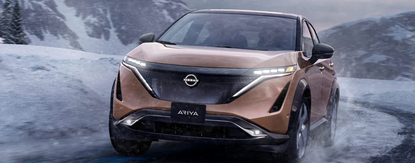 Orange 2023 Nissan Ariya driving down a snowy road.