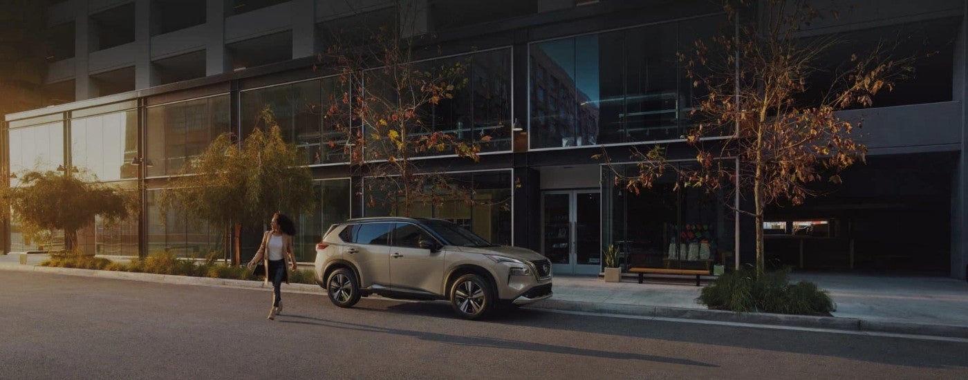 A person walking past a tan 2023 Nissan Rogue.