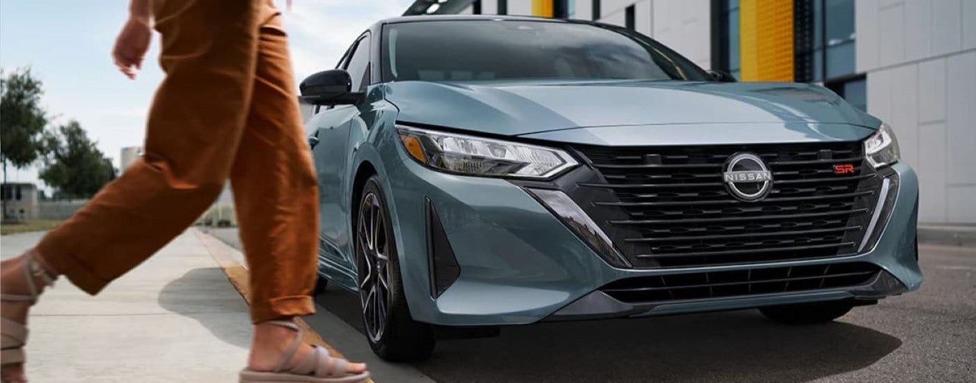 A person walking by a blue 2024 Nissan Sentra SR parked by a curb.