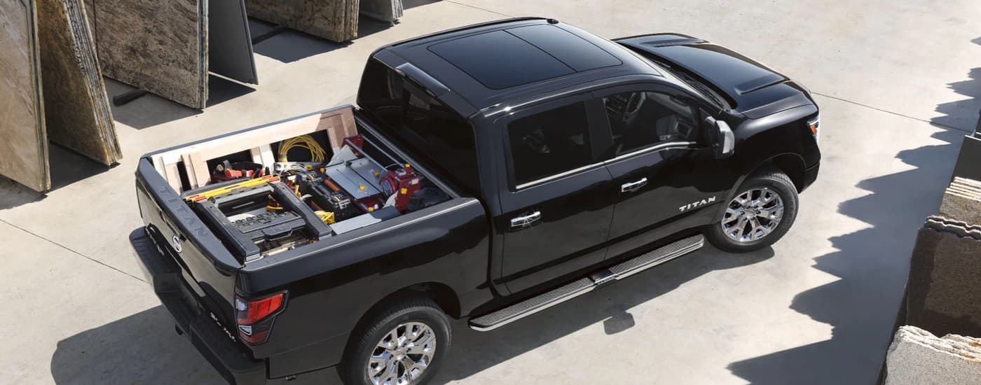 A black 2021 Nissan Titan is shown parked at a construction site with the bed full of cargo and tools.